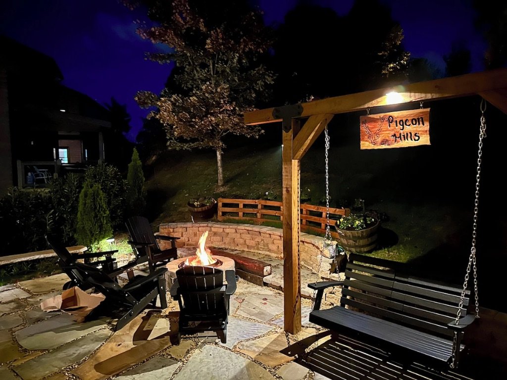 Pigeon Hills fire pit with Adirondack chairs porch swing and Pigeon Hills sign at night